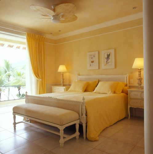 A suíte principal tem cama, cômodas e banquetas de estilo provençal. Piquê amarelo foi utilizado na confecção de colchas, cortinas e almofadas. Cama e banquetas da Secrets de Famille