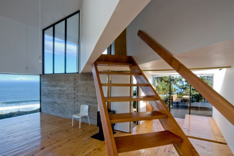Disposta em diagonal, a escada de madeira com corrimão é o maior destaque da parte interna da casa. As transparências deixam o papel de protagonista para a vista para o entorno