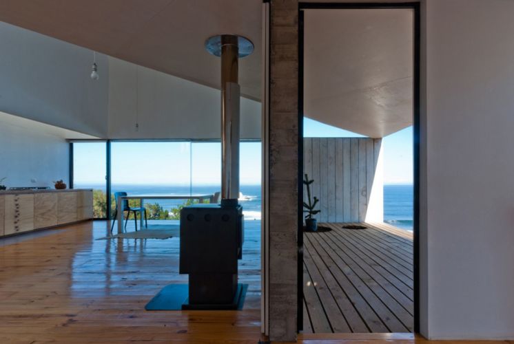 Vista a partir do quarto do térreo mostra os espaços integrados de estar, com lareira, jantar e cozinha, todos com vistas para o mar
